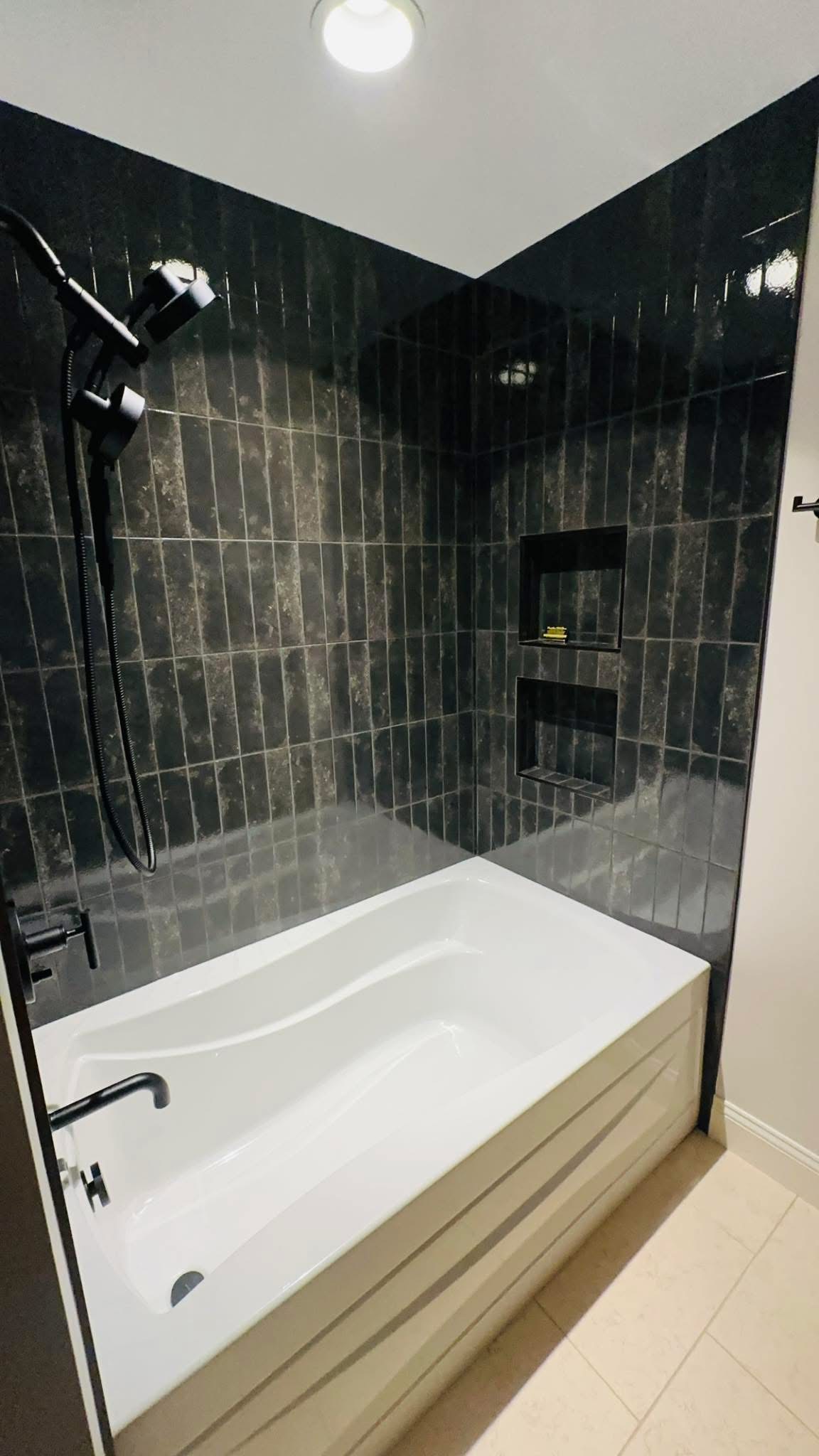 Glossy black tile tub surround with two recessed niches and matte black fixtures.